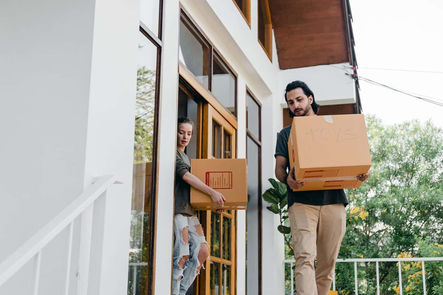 Two people carrying moving boxes into a house